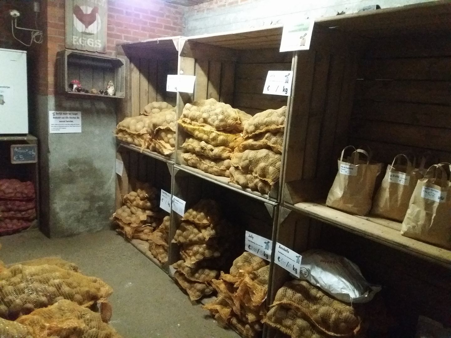 Een aantal rekken in de hoevewinkel van Raf Patat met verschillende soorten aardappelen verpakt in jutte zakken, klaar om mee genomen te worden.
